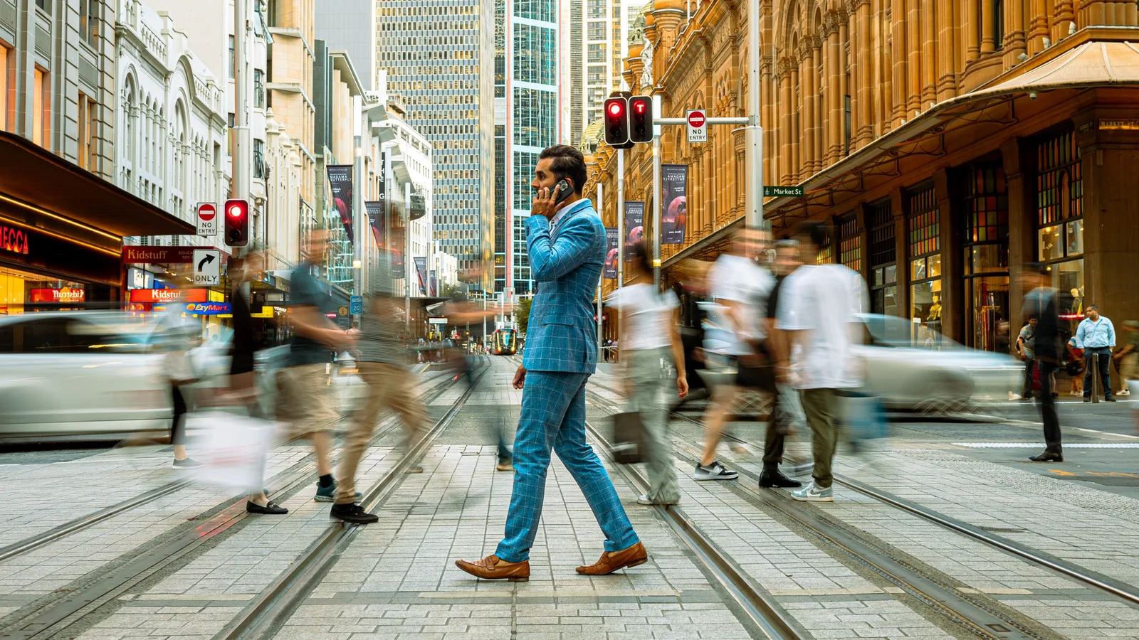 Businessman in a blue suit crosses a busy Sydney street, surrounded by motion-blurred pedestrians.